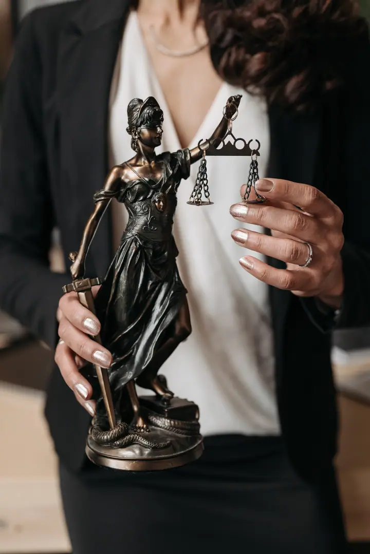 Estatuilla de la Justicia en bronce sostenida por una abogada con traje oscuro
